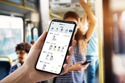 Young woman is standing on the bus using the phone and smiling.